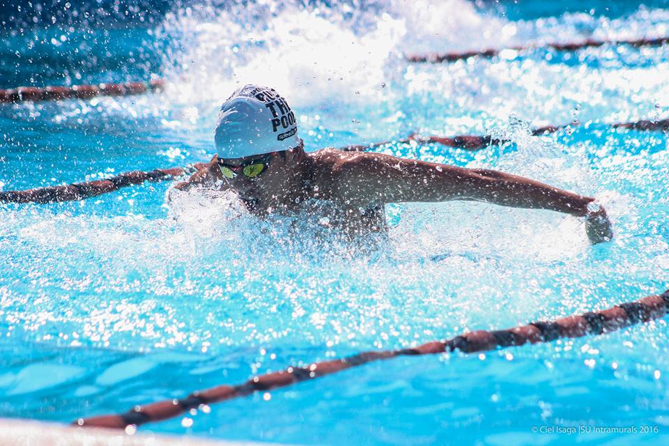 A swimmer mid-stroke in the butterfly, water splashing in a blue pool