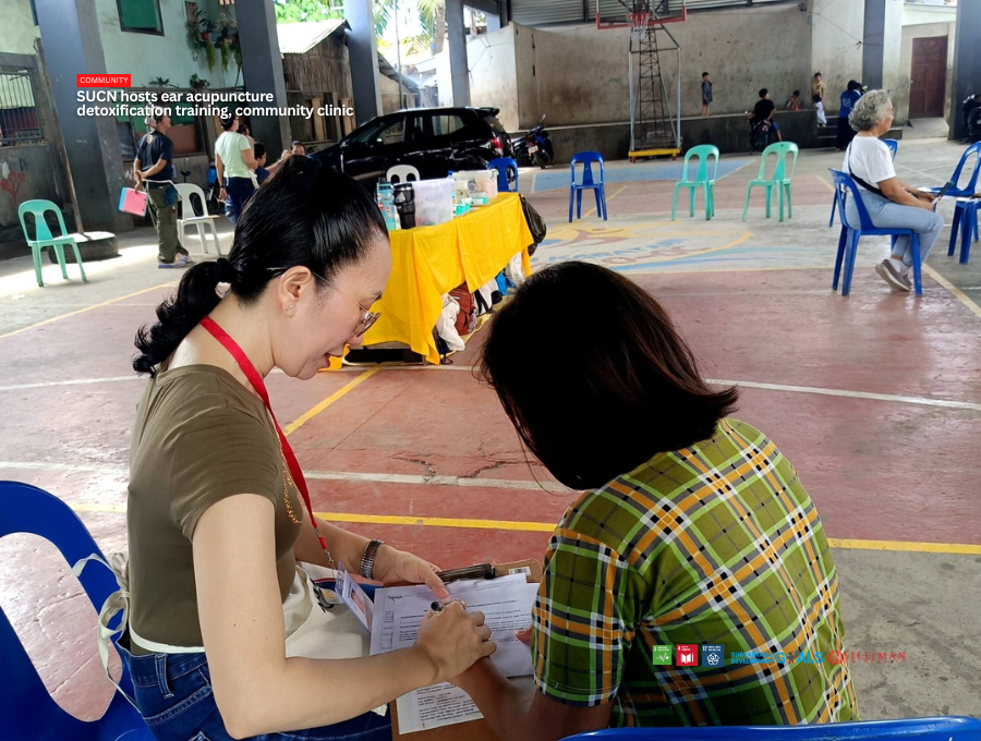 A participant assists a community resident during the registration and assessment process at the Barangay Lo-oc community clinic held as part of the Five-Day Ear Acupuncture Detoxification Training.